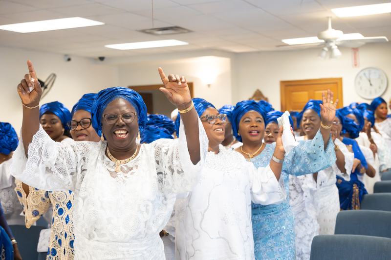Women in blue headwraps raising their hands in worship
